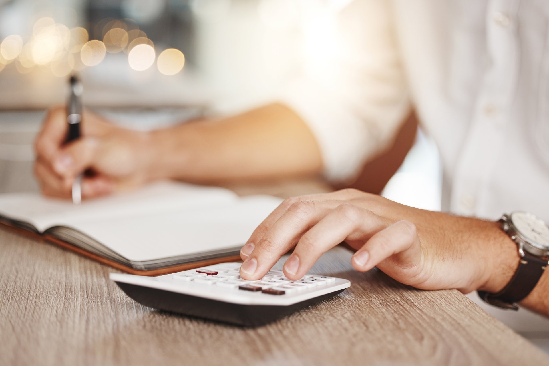 Mãos de contador usando calculadora e anotando valores para conferir a situação fiscal da empresa